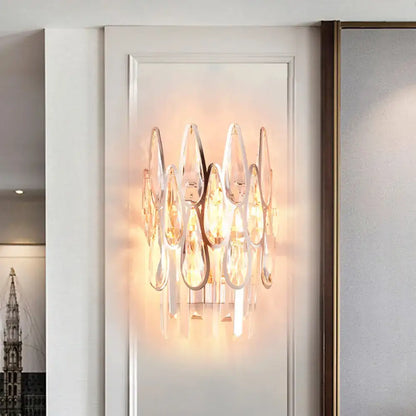 A modern gold finish wall lamp featuring teardrop crystal elements suspended from polished metal frames