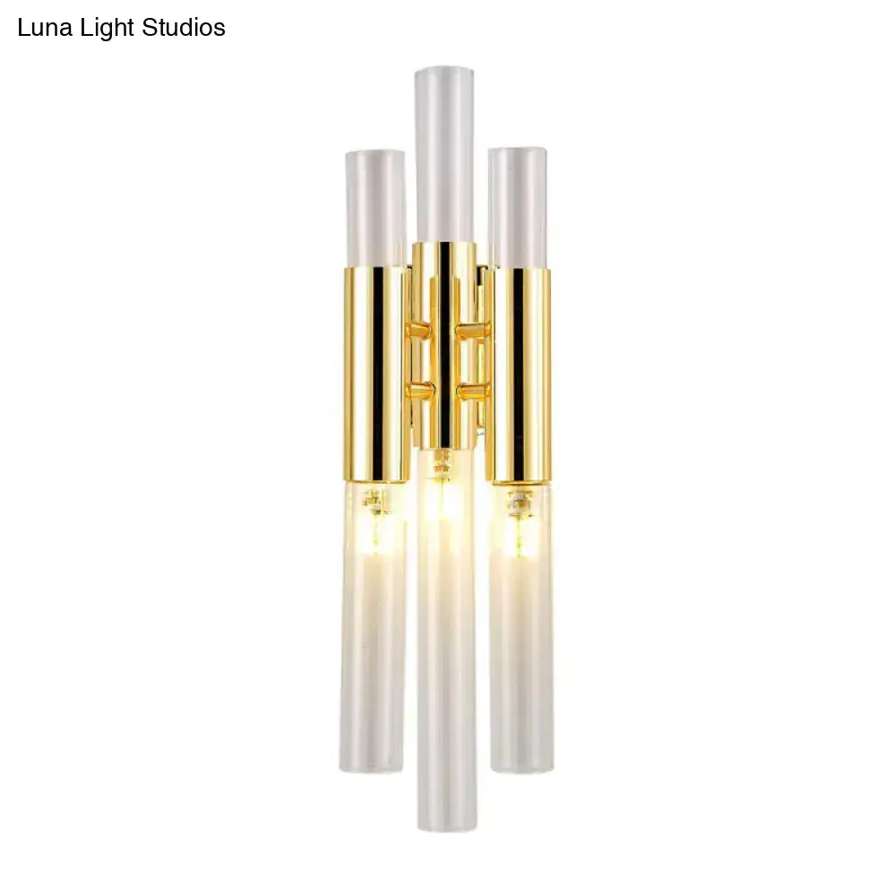 Modern gold living room wall sconce with three vertical frosted glass rods and warm glowing bulbs in metal frame