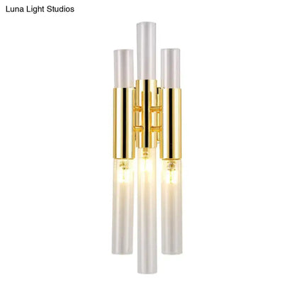 Modern gold living room wall sconce with three vertical frosted glass rods and warm glowing bulbs in metal frame