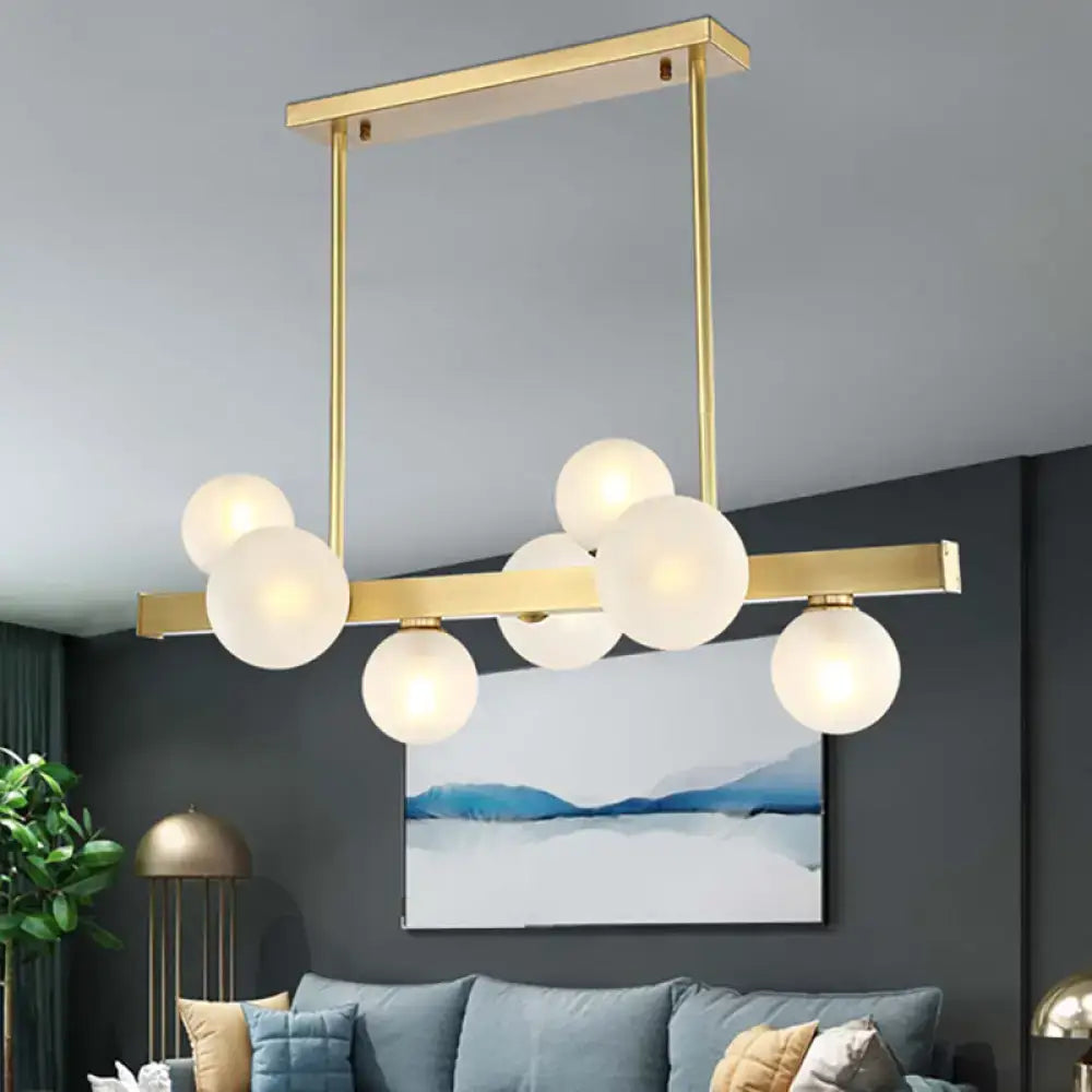 Modern gold pendant light with frosted glass globe bulbs in a linear design and adjustable chain cord length for dining room island