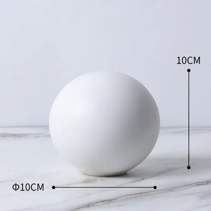 A smooth matte white ceramic sphere in a modern gold geometric cube round statue decor for living room