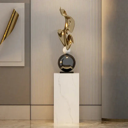 Modern gold geometric electroplating art sculpture with flowing forms on black sphere and white marble pedestal decorbites decor