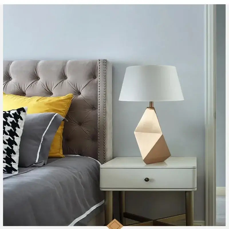 Modern gold geometric table lamp with three-dimensional gold-toned base and white fabric shade for bedroom use