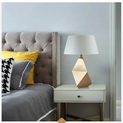 Modern gold geometric table lamp with three-dimensional gold-toned base and white fabric shade for bedroom use