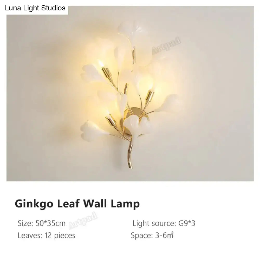 Modern gold ginkgo leaf porcelain wall sconce with 12 translucent white leaves and gold-toned metal stems emitting warm glow
