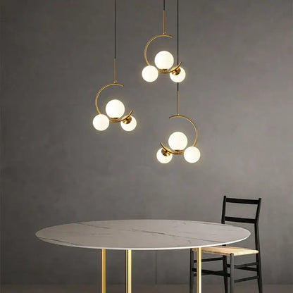 Three modern gold glass ball led chandelier pendant lights with spherical white glass bulbs hang above marble table