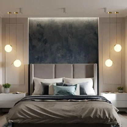 A modern bed with a tufted gray headboard and neutral bedding accented by teal pillows beneath a decorbites glass ball led pendant light