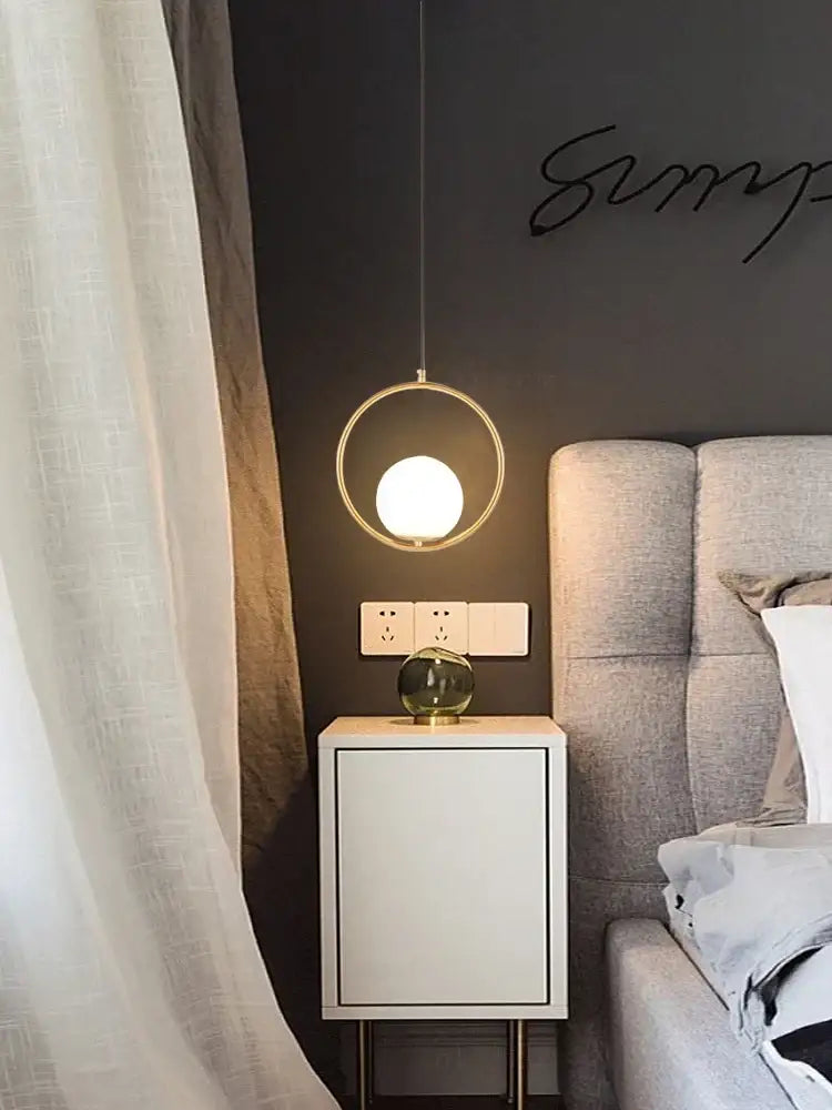 Modern gold glass ball led pendant light with a minimalist gold-toned frame and glowing bulb above a nightstand decorbites pendant light