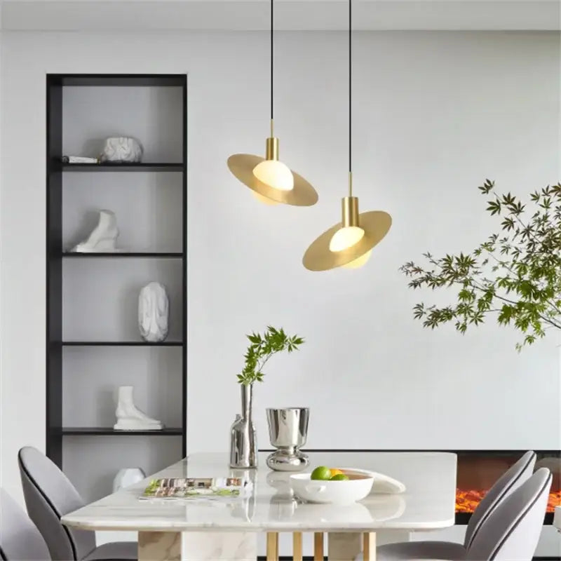 Two modern gold pendant lights with sleek disc-shaped glass ball led shades hang above a dining table decorbites pendant light