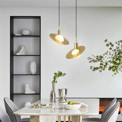 Two modern gold pendant lights with sleek disc-shaped glass ball led shades hang above a dining table decorbites pendant light