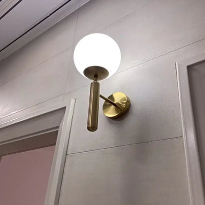 Modern gold glass ball mirror wall lights featuring a gold-toned wall sconce with a spherical white glass shade by decorbites