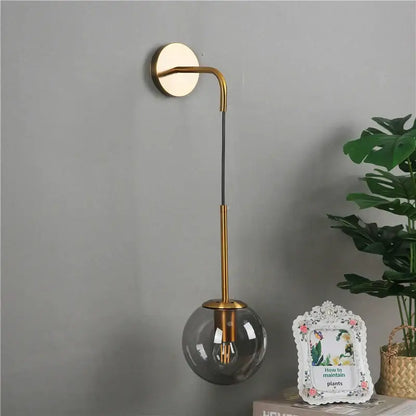 Modern gold glass ball wall lamp with a curved arm and smoked glass shade for elegant bedroom decorbites glass ball sconce