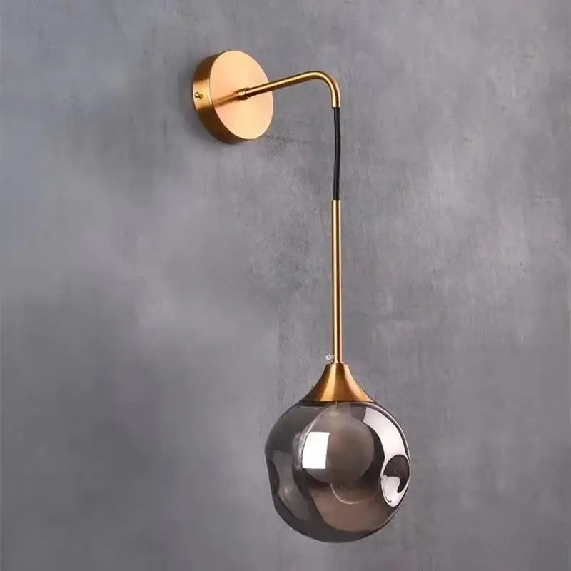 A sleek modern gold glass ball wall lamp with a curved arm and smoked decorbites glass ball globe