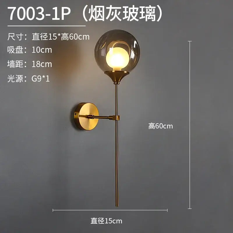 A sleek modern gold wall sconce with a smoked decorbites glass ball and slender brass stem for bedroom decor