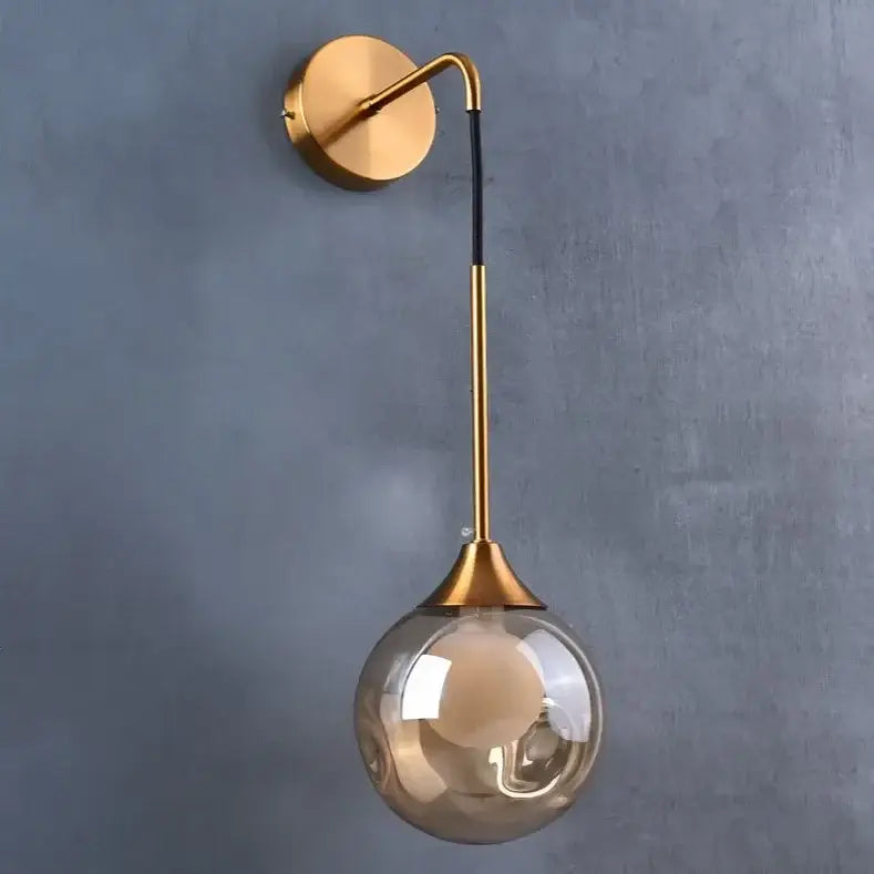 Modern gold wall sconce with a sleek curved arm and amber glass ball shade perfect for decorbites glass ball lighting