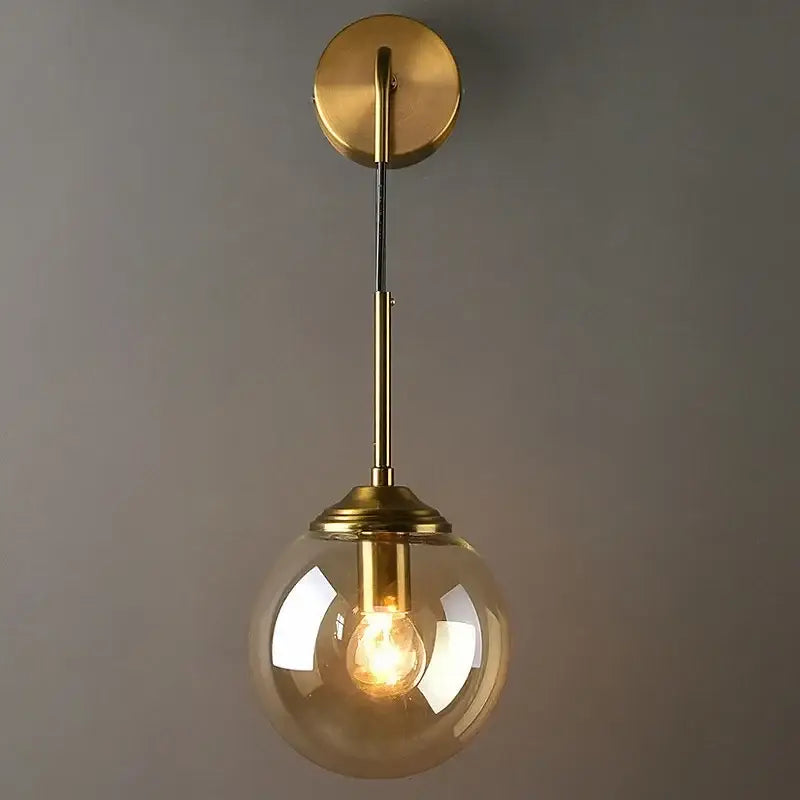 Modern gold glass ball wall sconce light fixture with brass finish and clear glass globe featuring exposed filament bulb