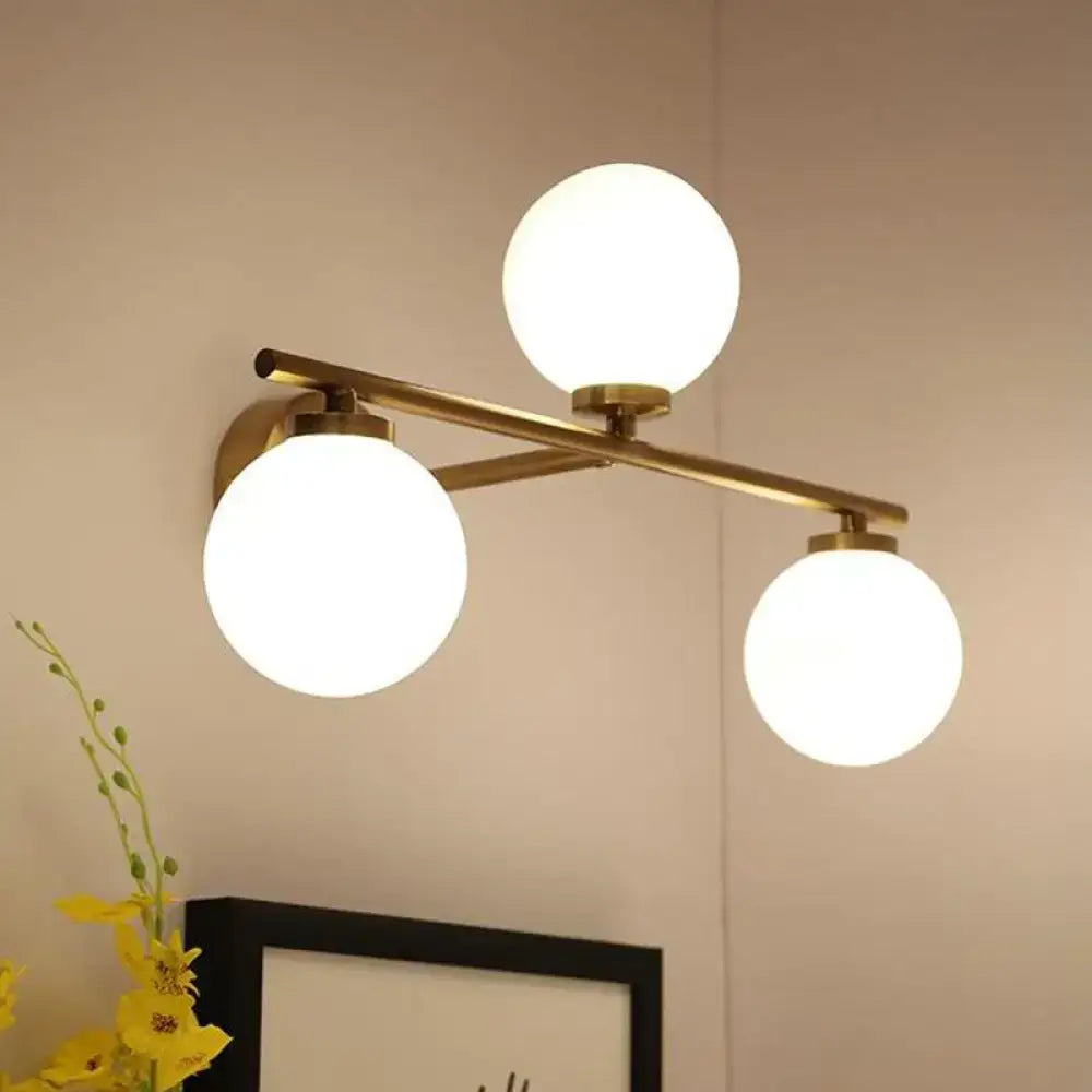 Modern gold wall lamp with brass finish and three frosted globe opal glass shades for bedroom lighting