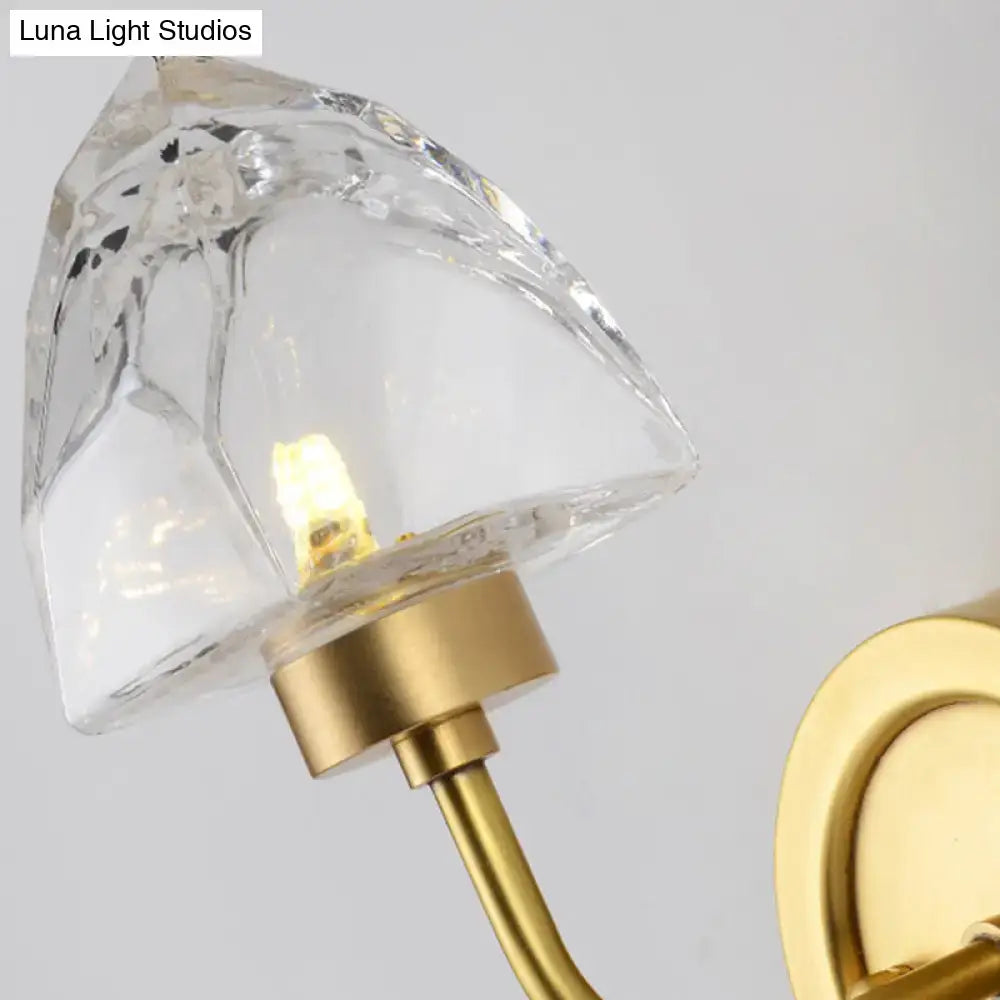 A modern gold ice cube wall light with a clear faceted crystal lampshade and gold-toned metal base and bracket