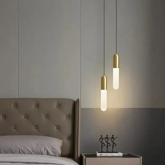 Two modern decorbites gold led pendant lamps with frosted glass cylinders and gold finished metal tops hang above bed