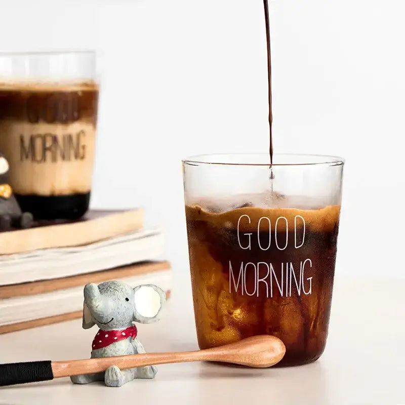 Modern gold letter decorbites glass breakfast cup filled with iced coffee being poured in clear glass cup with good morning text