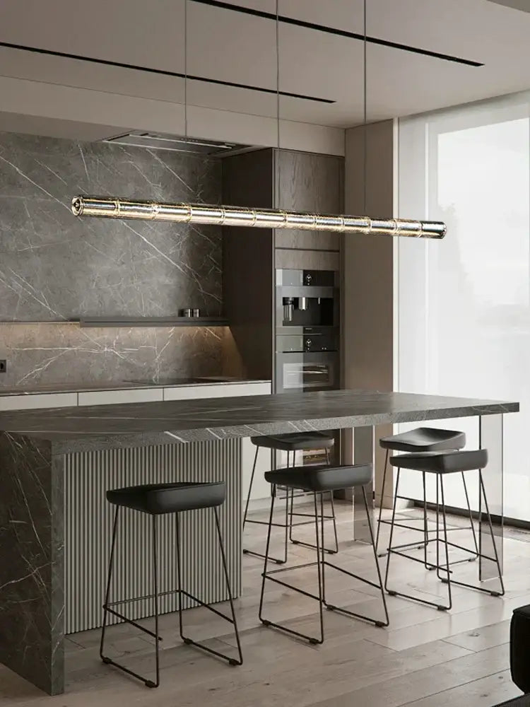 A sleek gold-toned glass led chandelier with a cylindrical design hangs above a kitchen island