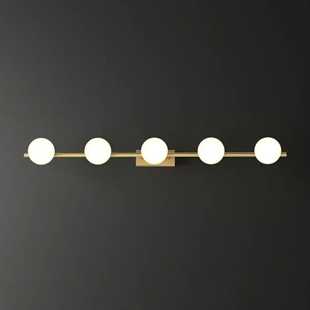 Modern gold linear wall sconce with five milky ball glass bulbs designed for bathroom lighting