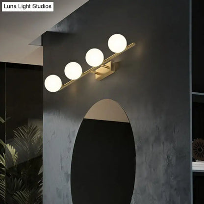 Modern gold linear wall sconce with four milky ball glass bulbs arranged diagonally for bathroom lighting