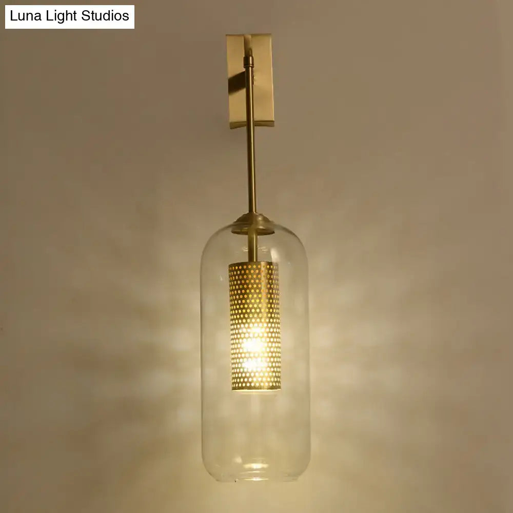 Modern gold mesh and clear glass sconce wall lamp with brass frame and illuminated perforated gold cylindrical shade