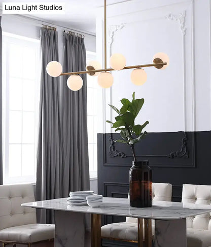 Modern gold metal pendant light with six warm-toned white glass globes for dining room island lighting