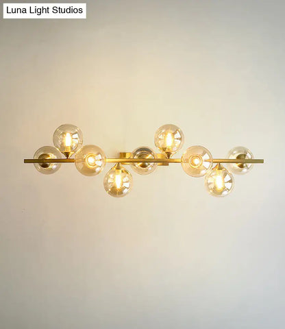 Modern gold metal wall sconce with multiple spherical amber glass bulbs on a horizontal bar for dining room lighting