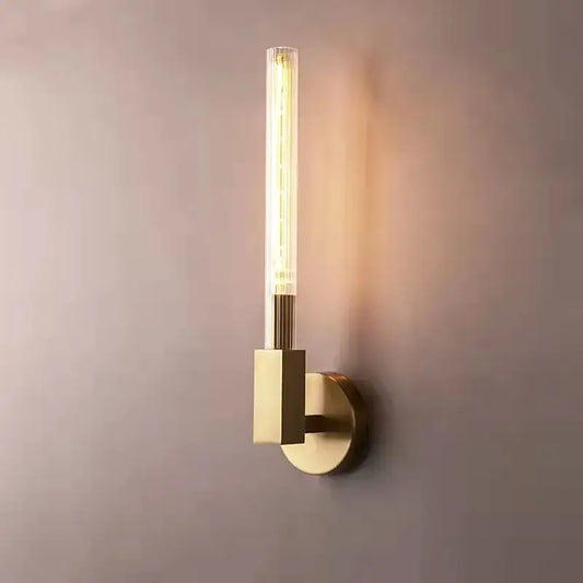 Modern gold metal and glass wall sconce light with brass finish and clear glass tube housing illuminated bulb for bathroom