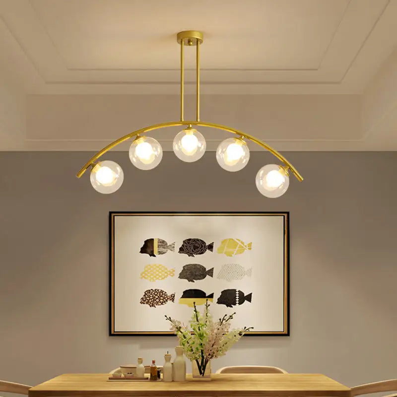 Modern gold metal ceiling light with five clear glass globe bulbs in an arched design for dining room use
