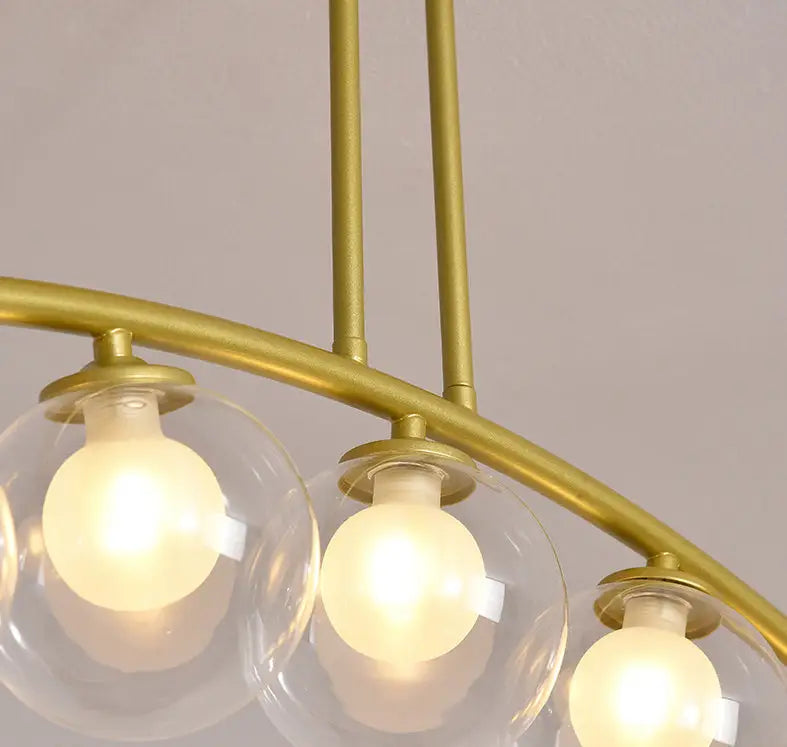 Modern gold metal arched ceiling light with three clear glass globes and warm bulbs for dining room illumination