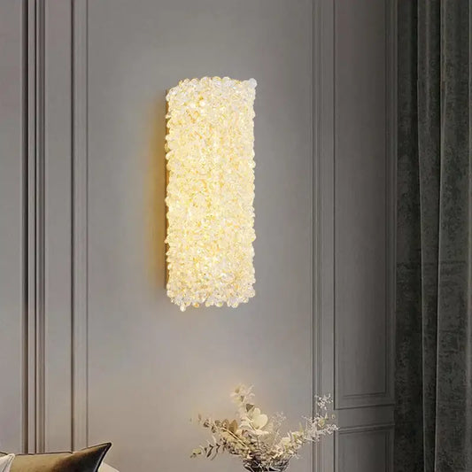 Modern gold metal crystal wall light featuring a rectangular sconce with clear faceted crystals emitting warm glow