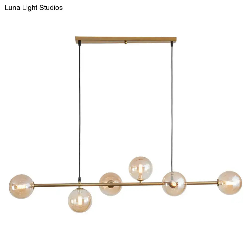 Modern gold metal island pendant light with five amber glass spheres suspended by black cords for dining room