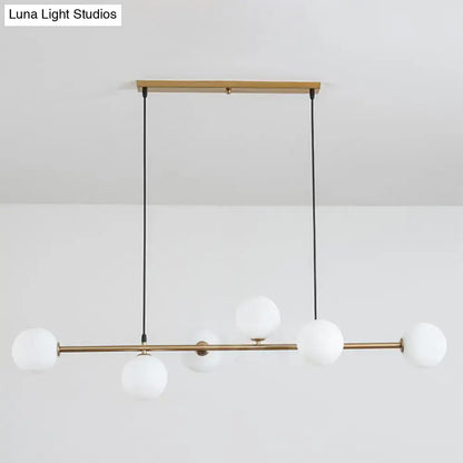 Modern gold metal island pendant with five frosted glass globes suspended by black cords from wooden ceiling mount