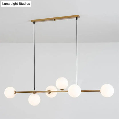 Modern gold metal island pendant with five frosted glass globes suspended by black cords for dining room lighting