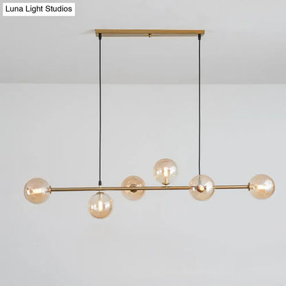 Modern gold metal island pendant light with five amber glass spheres suspended by black cords for dining room use