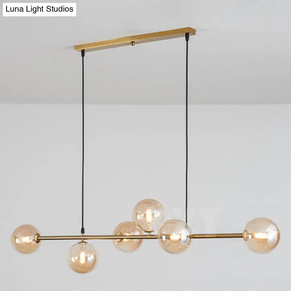 Modern gold metal island pendant with five amber glass globes suspended by black cords from a brass bar for dining room