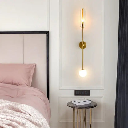 Modern gold metal wall light bedroom sconce featuring a gold-toned metal wall with frosted globe and cylindrical glass shade