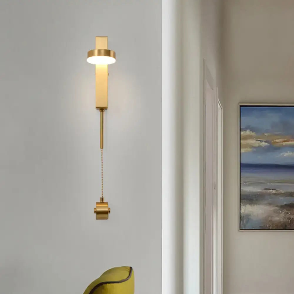 Modern gold metal wall sconce with cylindrical light fixture and pull-chain switch providing warm white light