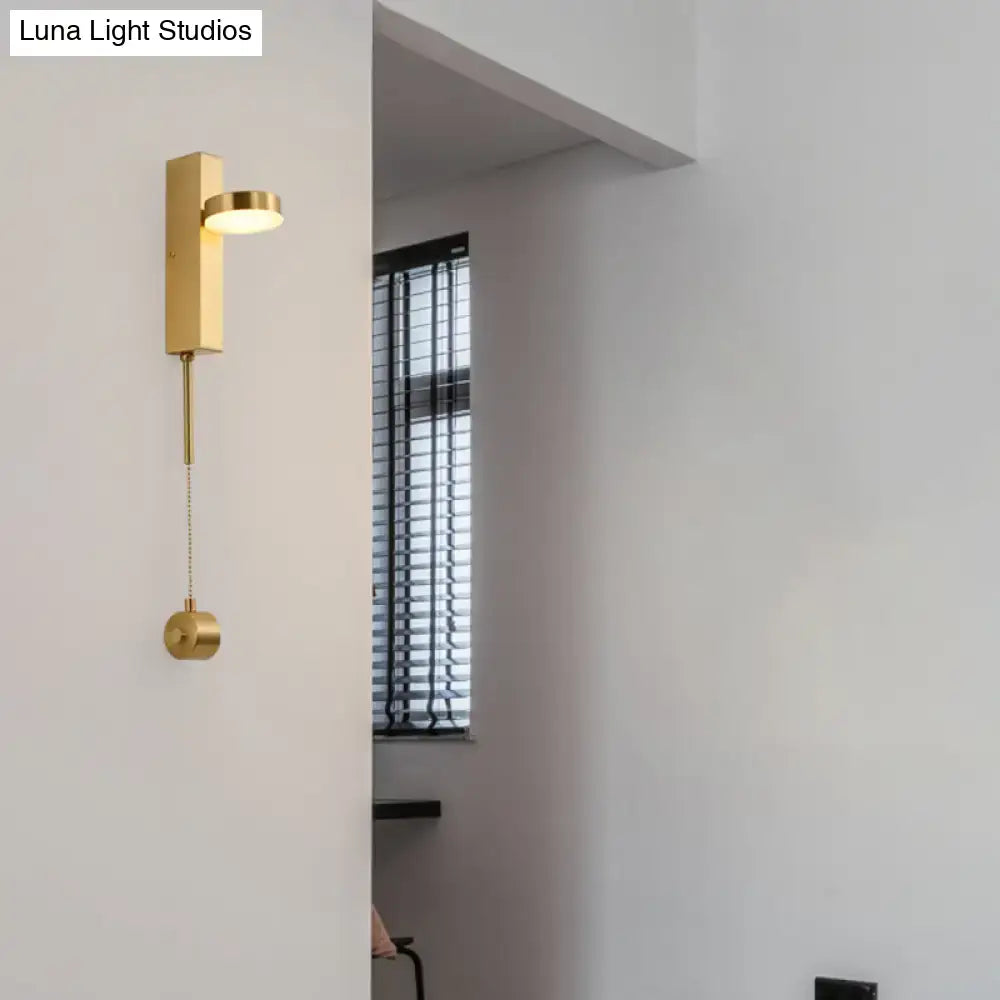 Modern gold metal wall sconce with a sleek rectangular base and adjustable circular head emitting warm white light