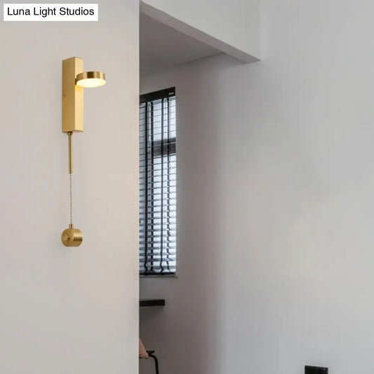 Modern gold metal wall sconce with a sleek rectangular base and adjustable circular head emitting warm white light