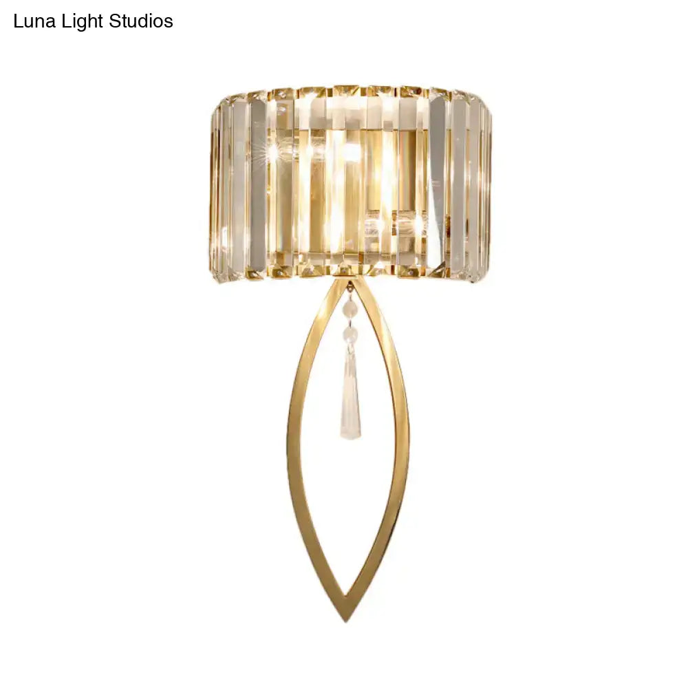 Modern gold metallic drum shade wall light featuring a gold-toned cylindrical crystal shade and elongated leaf frame