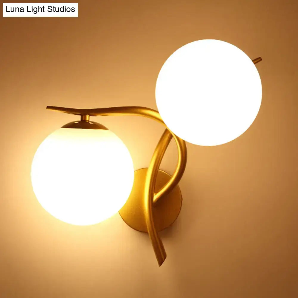 Modern gold wall sconce light with two glowing milk glass orb shades and standard bulb base for bedroom use