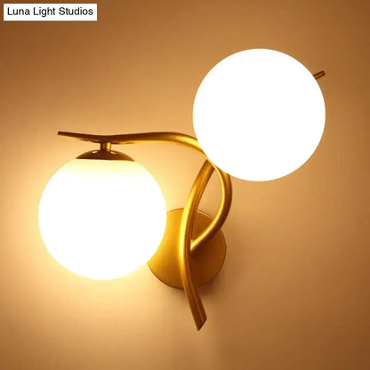 Modern gold wall sconce light with two glowing milk glass orb shades and standard bulb base for bedroom use