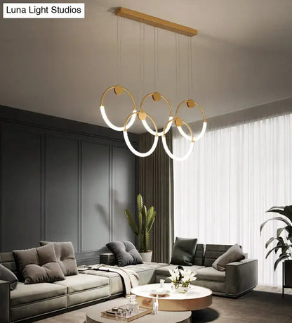 Modern gold minimalistic ring pendant light with three interlocking circular rings and wooden ceiling mount for living room