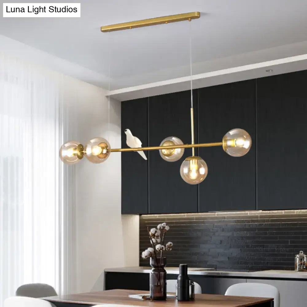 Gold-toned modo island pendant light with five spherical milk white glass bulbs and central decorative bird figurine for restaurants