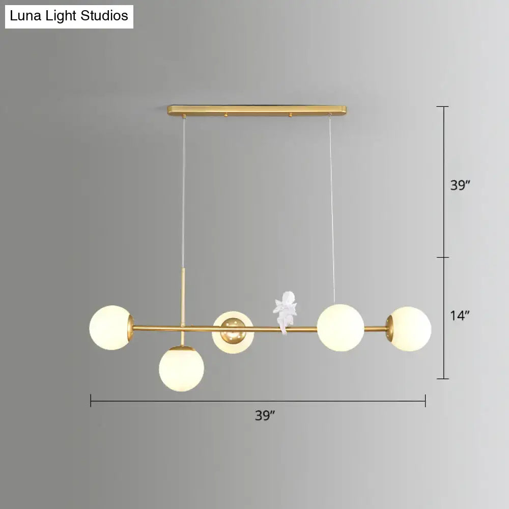 Modo island gold-toned pendant light with five frosted milk white glass globes and central decorative white figurine for restaurants