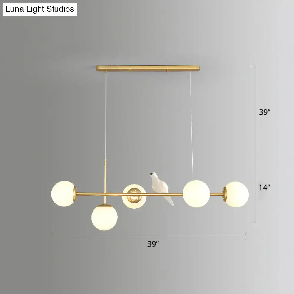 Gold-toned modo island pendant light with five frosted glass milk white globes and ceramic bird for restaurants